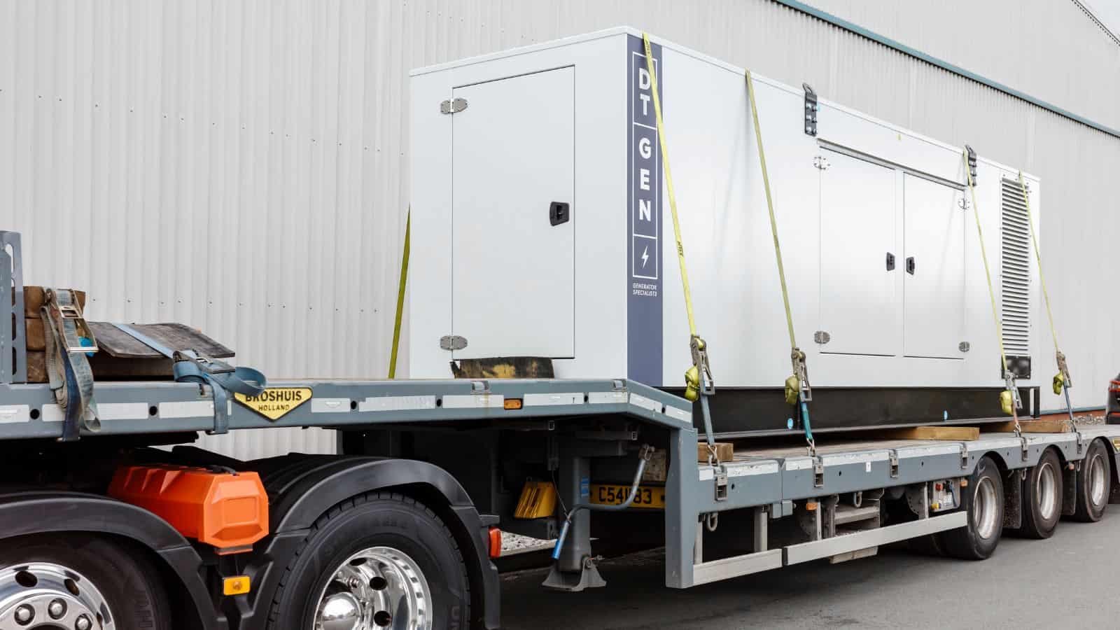 Enclosed industrial generator strapped to lowboy trailer for transport